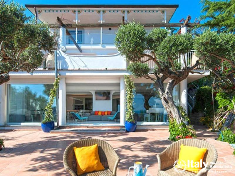 The beautiful front facade of the villa with a spacious patio and outdoor seating.