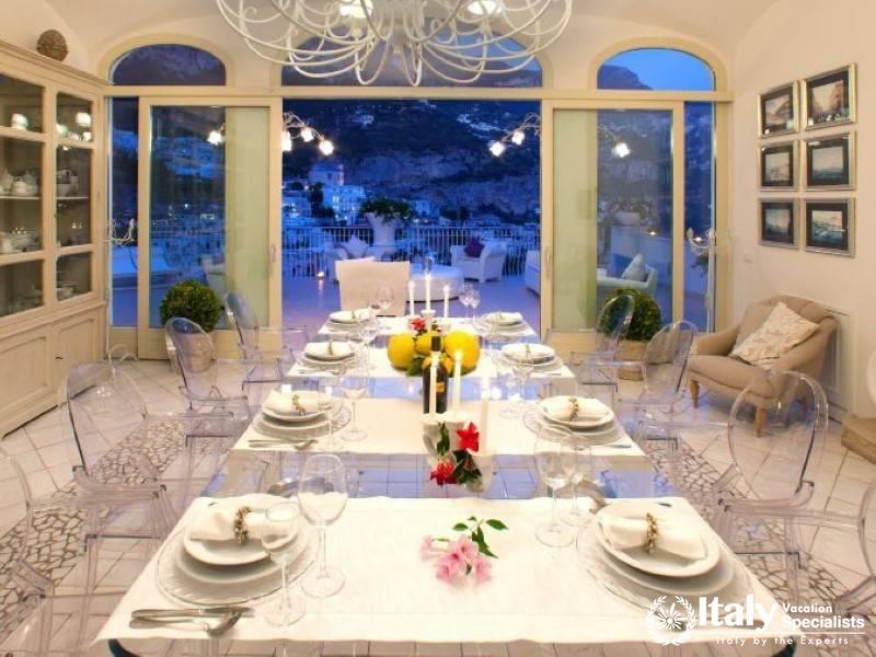 A beautifully set dining table with a panoramic view of Positano through large windows.