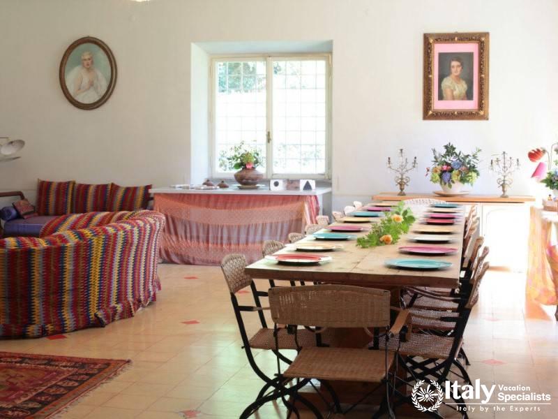 Dining room with a colorful sofa and long table set for guests.