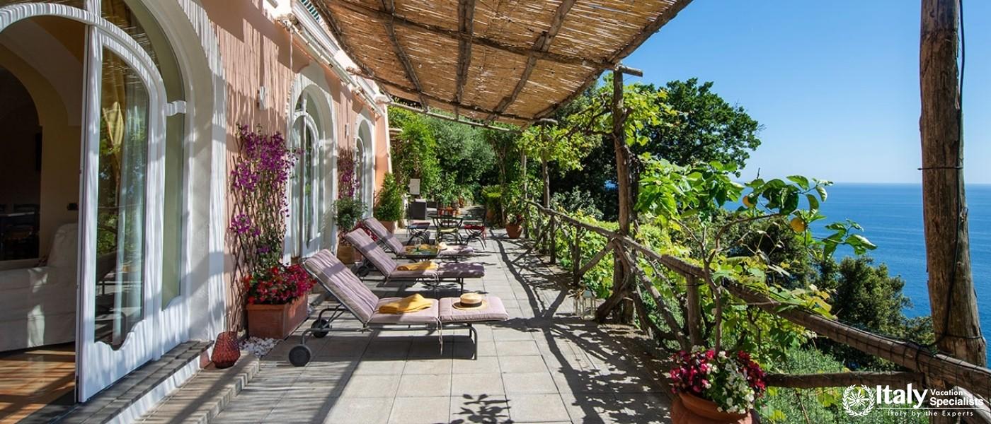 A charming sunlit terrace adorned with flowering plants and inviting lounge chairs, perfect for rela