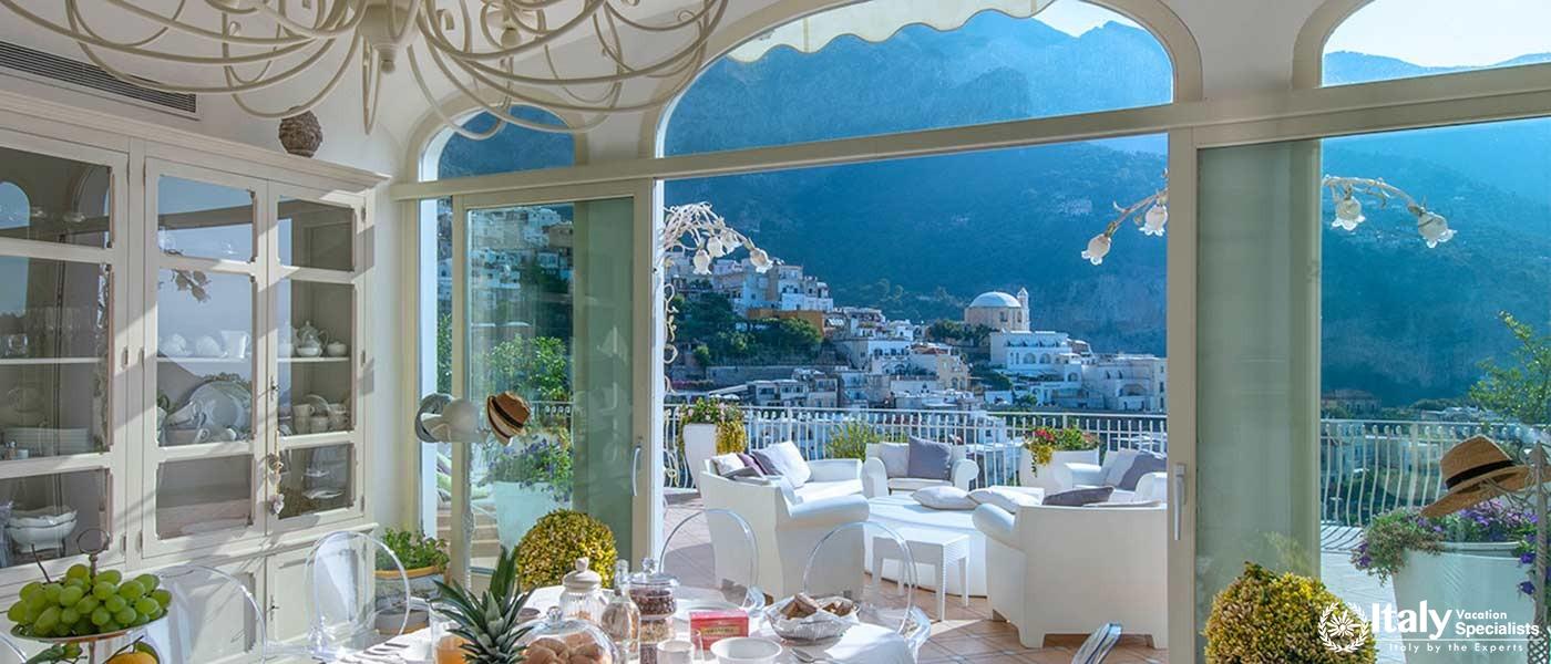 A bright and airy dining space with large windows offering panoramic views of Positano.