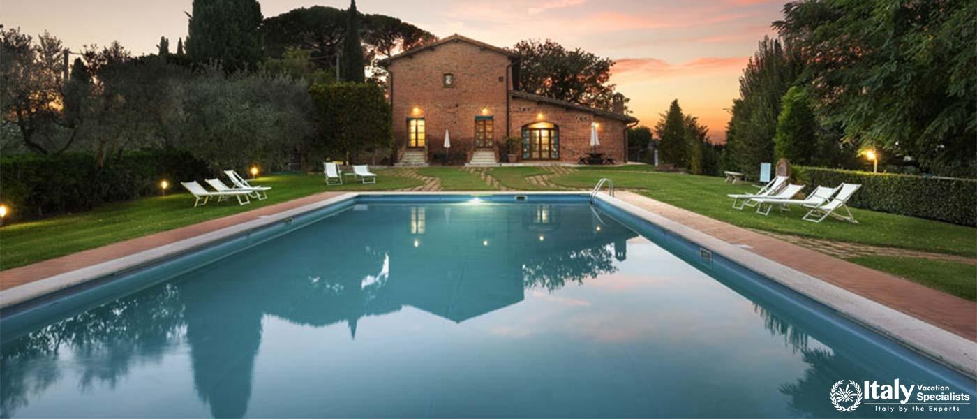 A Tuscan villa with a pool at sunset, surrounded by gardens.