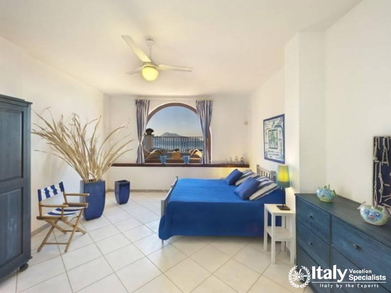 Spacious bedroom with ocean view through an arched window.