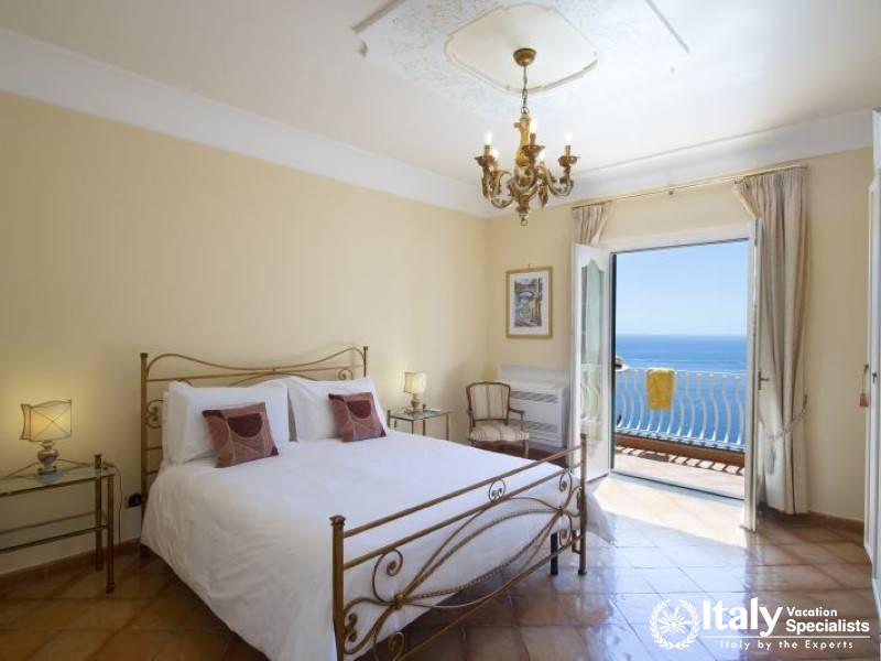 A serene bedroom with classic decor, opening to a private balcony with stunning sea views.