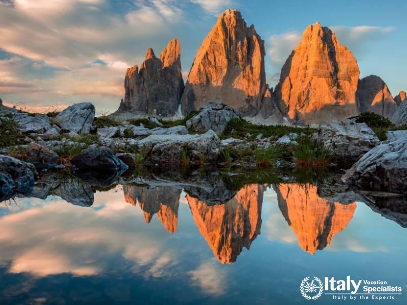 The iconic three peaks glowing at sunset, beautifully reflected in a tranquil alpine pond.