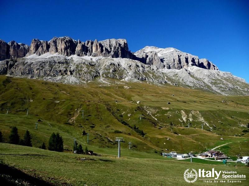 A sweeping view of Passo Pordoi, surrounded by rolling green hills and dramatic mountain peaks.