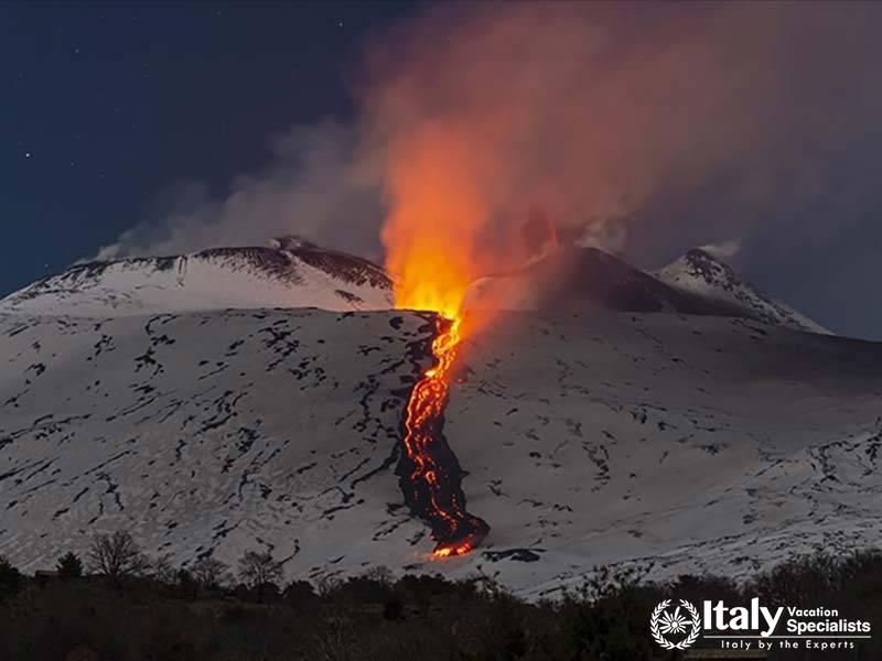 Dramatic shot of Mount Etna erupting at night, with bright lava flowing down its snow-covered slopes