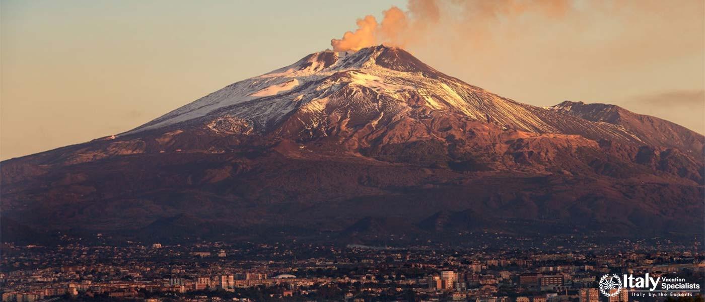 Mount Etna spewing smoke, showcasing its active volcanic nature with the city of Catania below